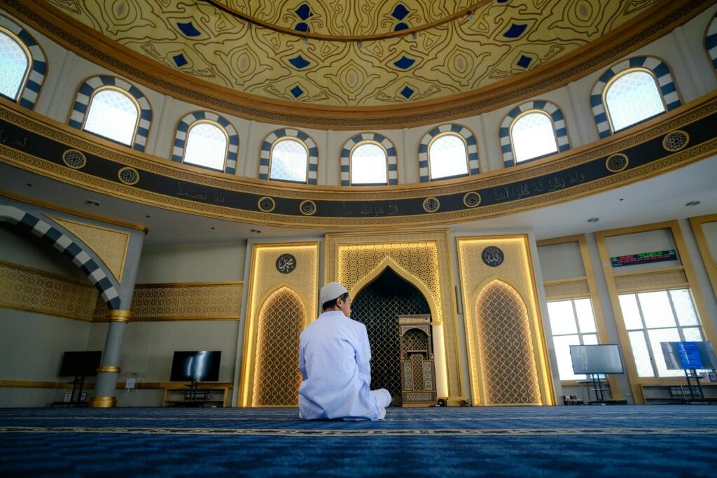 pexels-photo-36495071-36495071 A man in traditional clothing prays inside a stunning mosque interior, embracing spiritual peace.