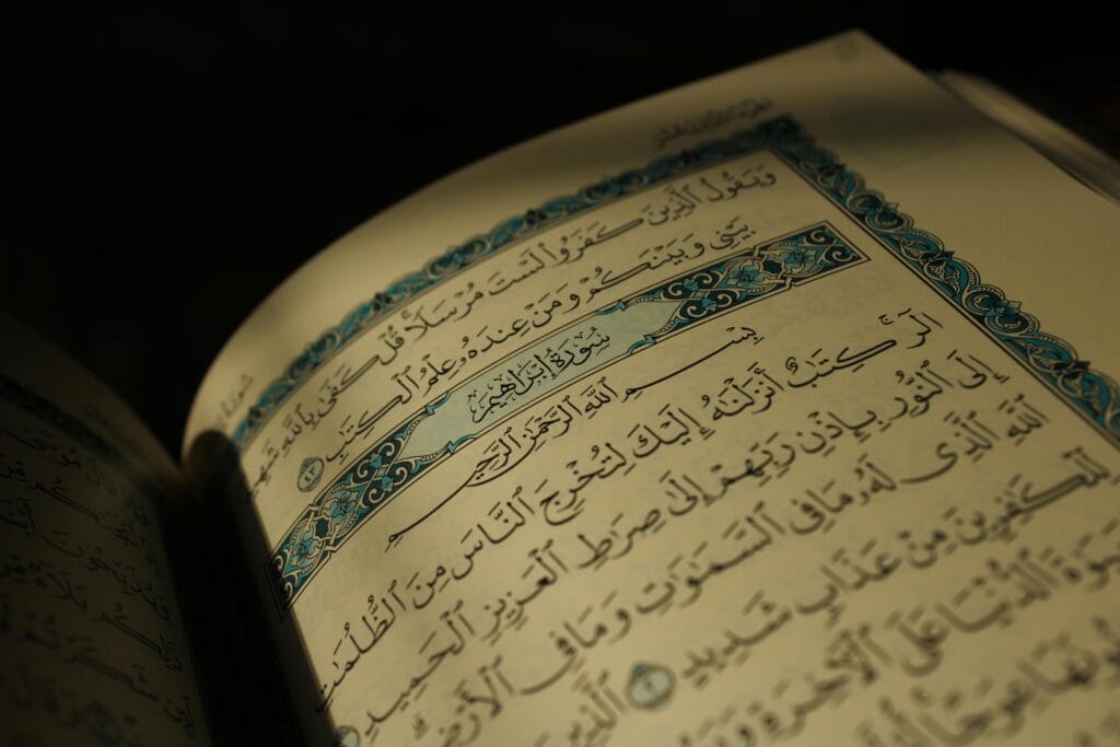 pexels-photo-36188877-36188877 Close-up of an open Quran displaying Arabic calligraphy under warm lighting, conveying spirituality.