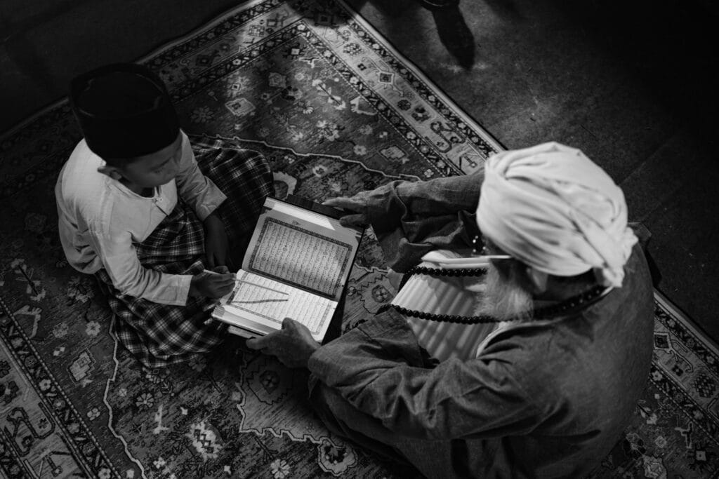 pexels-photo-36451942-36451942 Black and white image of a boy learning from an elder, highlighting traditional Islamic education in Jakarta.