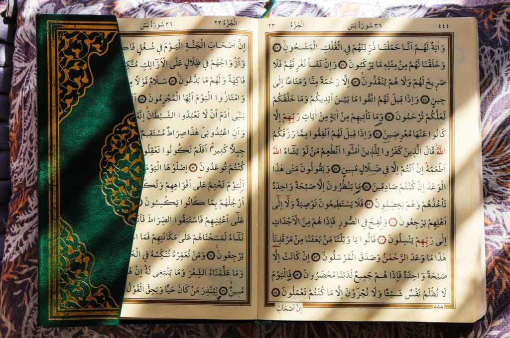 pexels-photo-36521597-36521597 An open Quran with a green decorative cover, illuminated by sunlight, showing Arabic script.